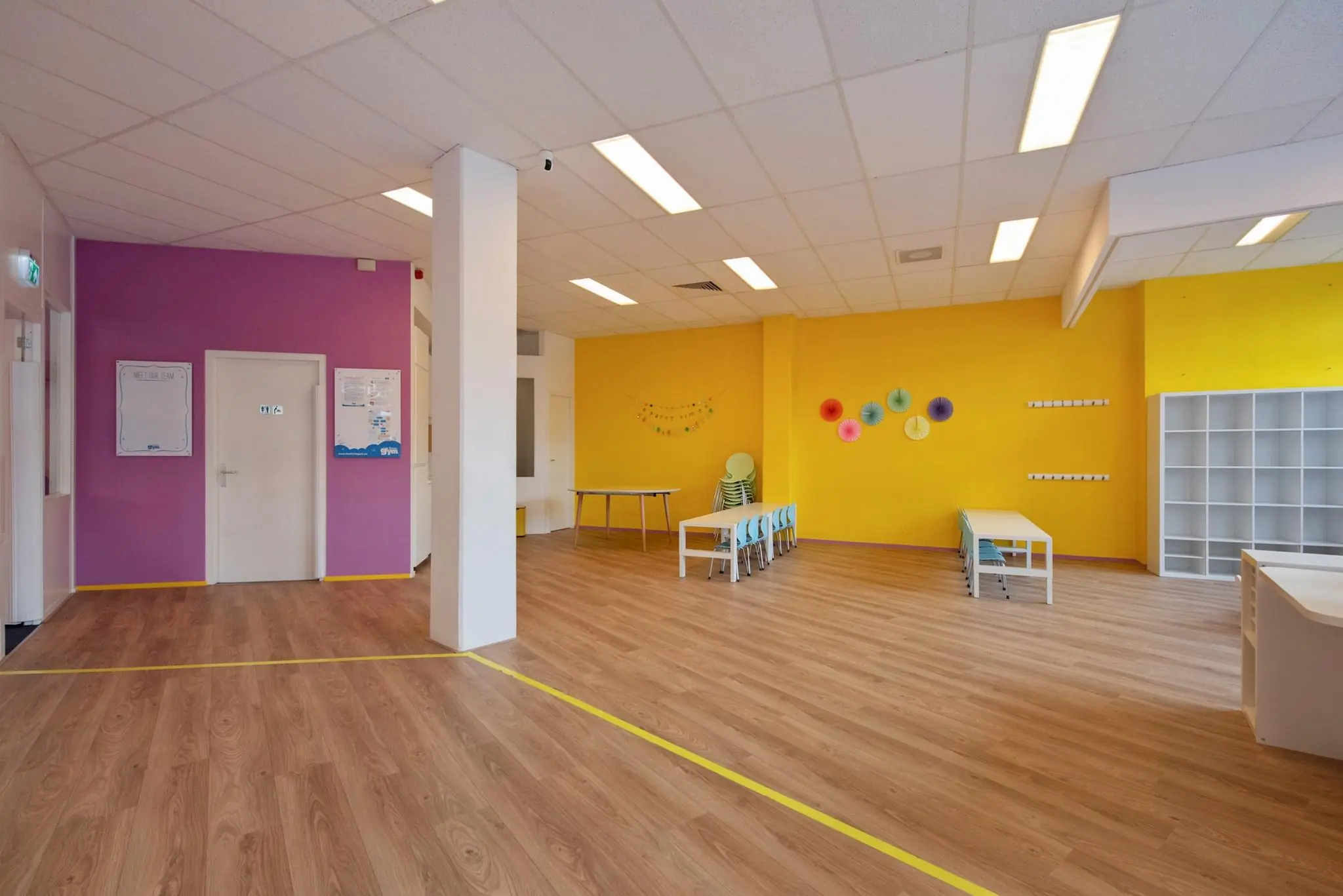 Kleurrijk en ruim lokaal in een kinderdagverblijf aan de Koningin Julianalaan met tafels, stoelen en vrolijke wanddecoratie.